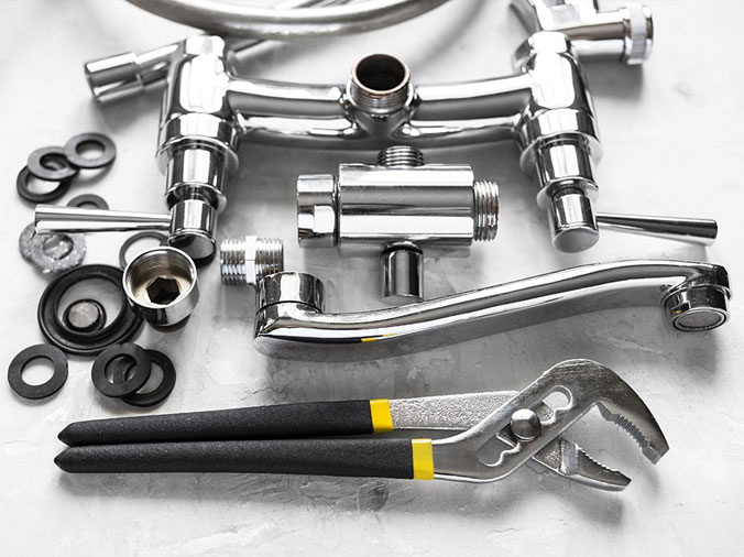Disassembled chrome sink faucet and a plumbing wrench